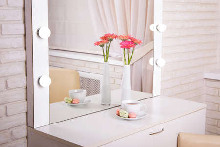 Client's place in hairdressing and beauty salon with cup of tea, macaroons and pink gerbera in vaseの写真素材