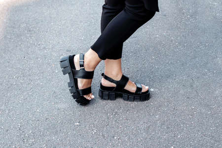 Female legs in black fashion and stylish boots with beautiful pedicure nails on gray road background