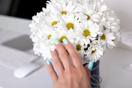 Beautiful female hand with blue manicure nails on chamomile flowers backgroundの写真素材