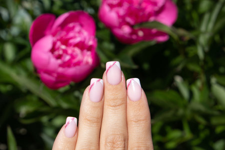 Beautiful female hand with pink manicure nails on peonies flower backgroundの写真素材