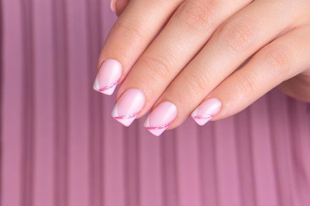 Beautiful female hand with pink and white manicure nails, sparkling french designの写真素材