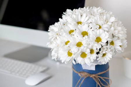 Beautiful bouquet of chamomile flowers on office desk near computerの写真素材