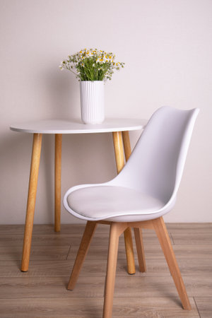 Modern white leather chair, table and chamomile flowers in vase in apartmentの写真素材