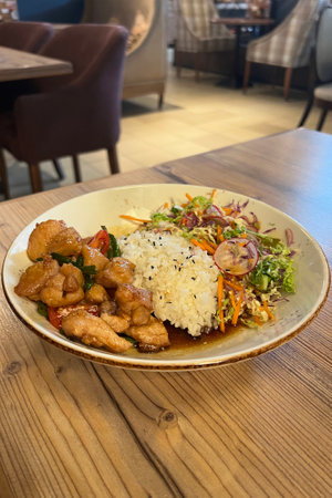 Rice with chicken, tomatoes and cucumber on plate in restaurantの写真素材