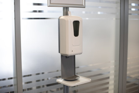 White plastic dispenser for antivirus and antibacterial hand washing, hanging near the door....