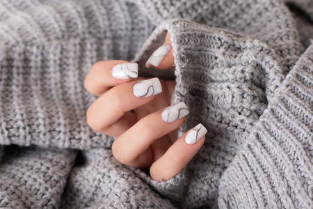 Beautiful female hand with beige and gray manicure nails on wool backgroundの写真素材