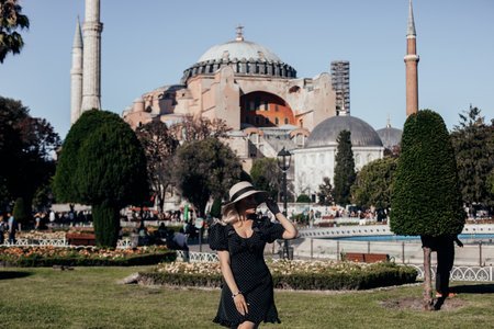 Young stylish woman in black polka dot dress and hat walking in park near Hagia Sophia mosque in Istanbul, Turkeyの写真素材