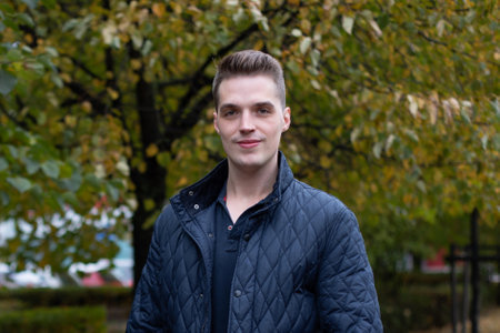 Portrait of young handsome man in blue jacket in park
