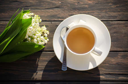 Hot tea in a white cup with a bouquet of flowers on a wooden backgroundの写真素材