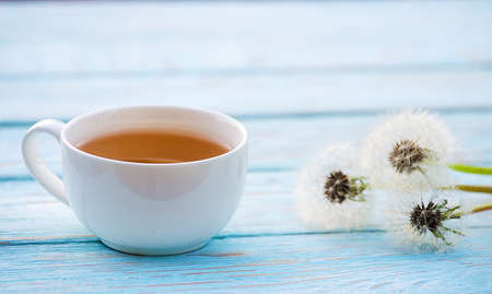 Hot tea with a bouquet of dandelions on wooden backgroundの写真素材
