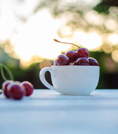 Sweet cherries in a cup on a wooden table and sun raysの写真素材