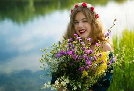 Happy girl on the field collects flowers for a bouquetの写真素材