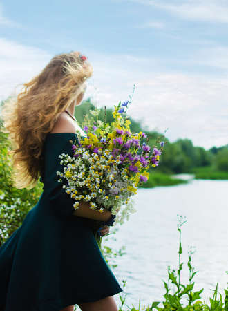 Happy girl on the field collects flowers for a bouquetの写真素材