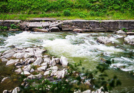 A stream in the mountains flows along the rocks and a stormy waterfall in the summer