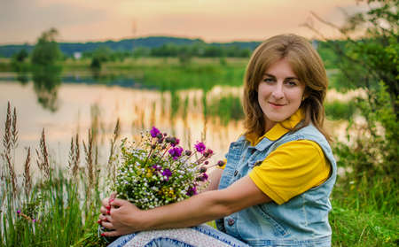 Happy girl on the field collects flowers for a bouquetの写真素材