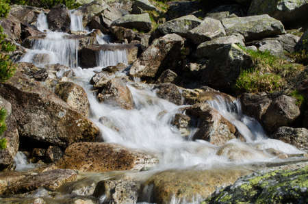 A stream in the mountains flows along the rocks and a stormy waterfall in the summerの写真素材