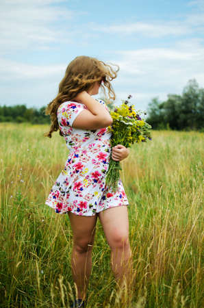 Happy girl on the field collects flowers for a bouquetの写真素材