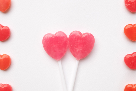 Pink Valentine's day heart shape lollipop with small red candy in cute pattern on empty white paper background. Love Concept. colorful hipster style. Knolling top view.の写真素材