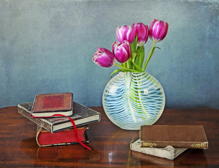 Interior still life:glass vase with pink tulips and ancient books on a wooden tableの写真素材