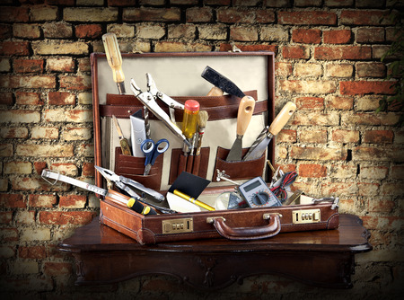 An assortment of services and maintenance tools in a leather case against a grunge brick background