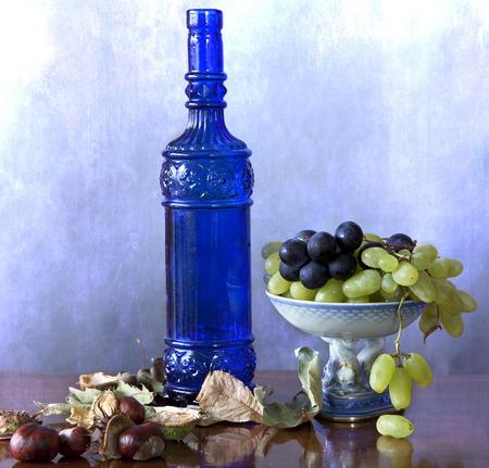 Still life: blue glass bottle with autumnal fruits, grapes and chestnuts, and leavesの写真素材