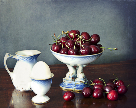Bowl of red and ripe cherries on a wooden table, a milk jug and a boiled egg on a eggcup