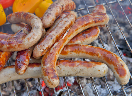 Sausage and peppers grilled by ember fire on a portable barbecue grill outdoor.の写真素材