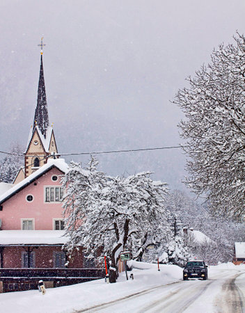 Snowfall on Austrian route, a car proceeds carefully on the white route near an idyllic villageのeditorial素材