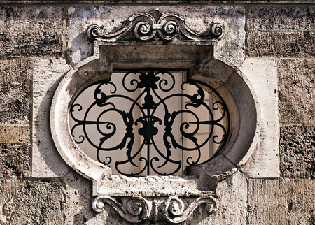 decorated marble frame closed by iron decorated grille on stone wallの写真素材