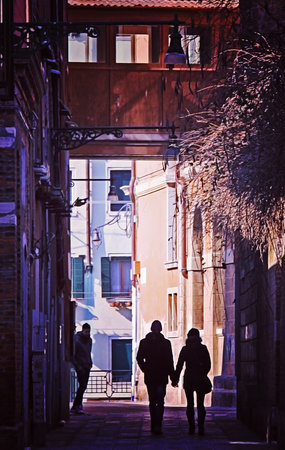 Venice, Italy - silhouette of a couple walking hand in hand through the narrow streets of Venice on a sunny day. Vintage effect added.のeditorial素材