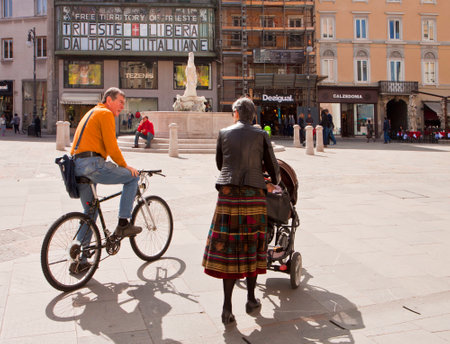 Trieste, Italy - Exchange Square Piazza della Borsa, man in bike and woman with baby stroller chat pleasantly on the square enjoying the spring  sunny dayのeditorial素材