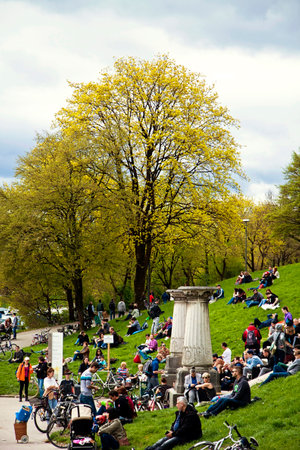 Munich, Germany - people in a festive day of spring sitting leisurely on green lawn and stairs at Bavaria park with the view of flowering treesのeditorial素材