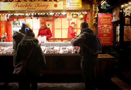 Munich, Germany - festive atmosphere at Residenz Kaiserhof Christmas market illuminated at night, crowded with tourists and residents, here a kiosk selling candies and frozen chocolate fruitsのeditorial素材