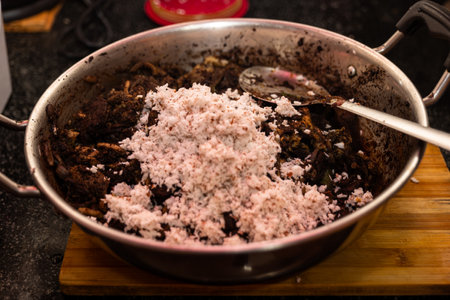 A close-up photo of mutton meat and blood being fried in a pan with coconut milk. The cook is adding more coconut milk to the pan, and the mixture is bubbling and sizzlingの写真素材