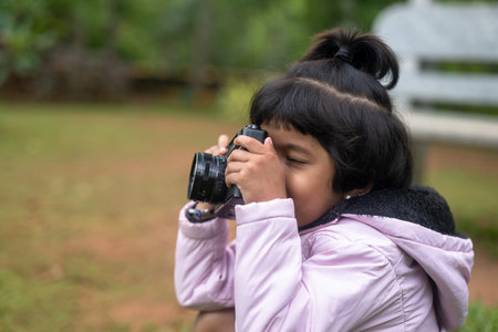 A young girl, about 6 years old, is holding a DSLR camera and taking a photo. She is wearing a pink dress.の写真素材