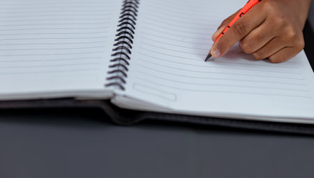A close-up photo of a kid, writing in a notebook. He is left-handed and his hand