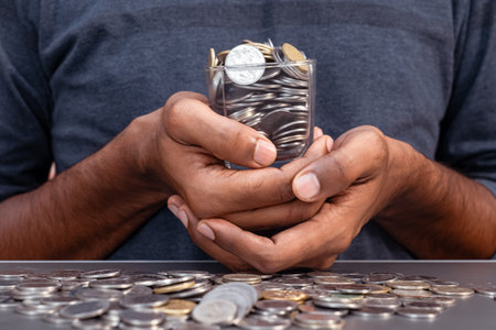 A man in traditional Indian clothing is holding a handful of Indian coins in both hands. The coins are spread out on a glass table in front of himの写真素材