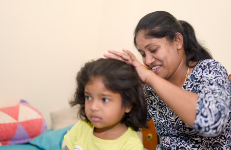 Indian mother combing her daughter's hair in the living room.