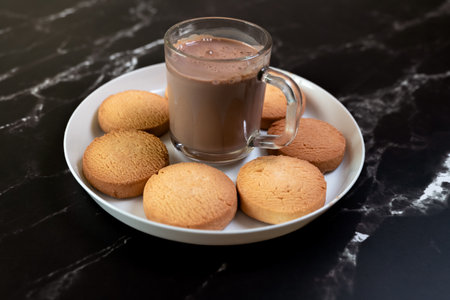 Cup of hot chocolate and cookies on a white plate on a black marble background
