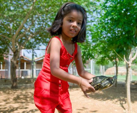 Little girl in a red dress playing with a turtle in the parkの写真素材