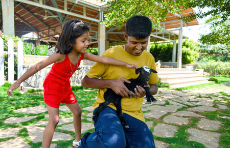 Father and daughter playing with a goat in the garden. Concept of friendly family.の写真素材