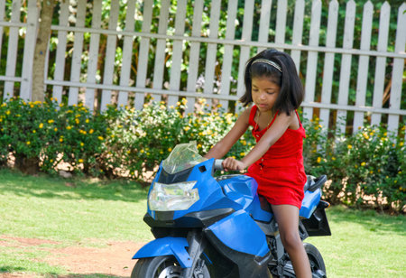 Cute little girl riding a motorbike in the garden on a sunny dayの写真素材