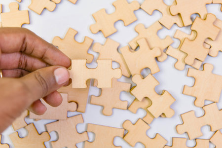 Close up of human hand putting jigsaw puzzle piece on white backgroundの写真素材