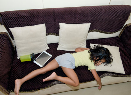 Top view of young woman lying on sofa and using digital tablet.