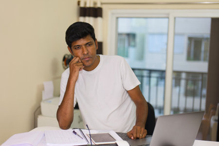 young attractive and concentrated indian man working on computer laptop at home office desk in deeply thinking conceptの写真素材
