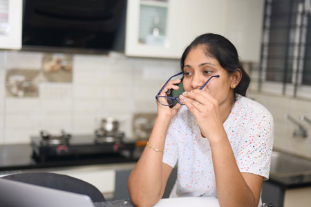 Young woman in the kitchen at home, she is using a laptop computer. wearing eyeglass