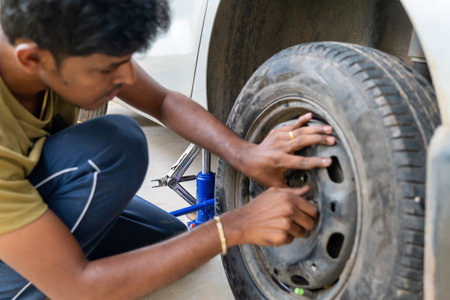 Focused individual manually removes lug nuts from a car tyre using a hand tool. Essential automotive care.の写真素材