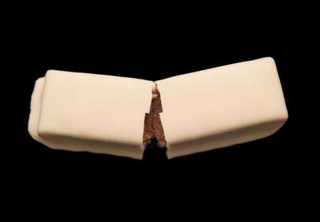 A split white chocolate bar reveals a luscious caramel center against a dramatic black background.の写真素材