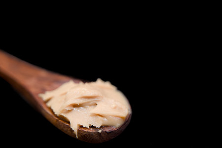close up of a wooden spoon with peanut butter on a black background