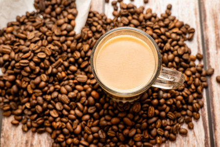Inviting espresso in a clear mug, surrounded by roasted coffee beans on a rustic wooden surface.